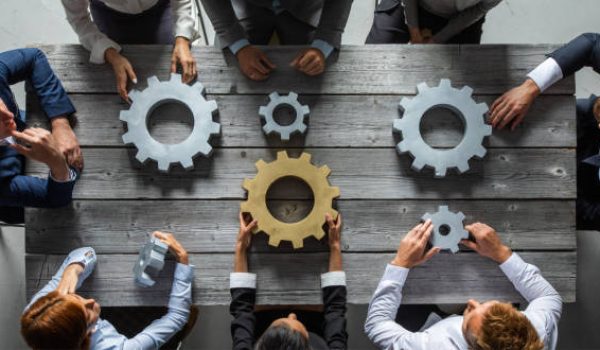 Group of business people joining together silver and golden colored gears on table at workplace top view