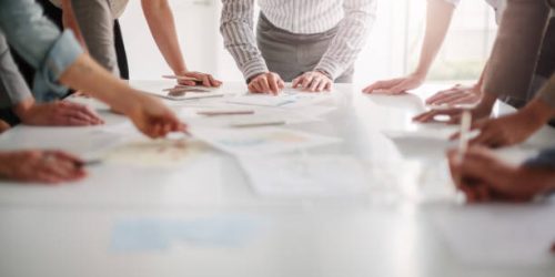 Low angle view of hands of multiracial group of people working with ideas and brainstorming together to make decisions with documents on table in creative office teamwork